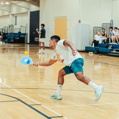 Student playing pickleball on the Rec court while more students watch